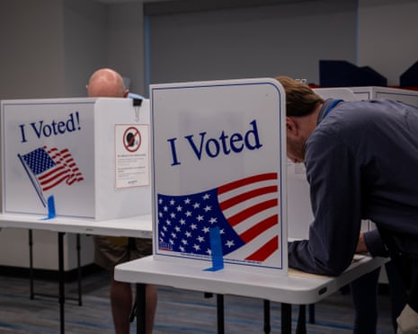 Voters cast ballots at booths displaying "I Voted" signs with American flags, Arlington, Virginia