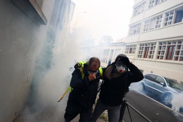 Two masked demonstrators cover their faces amid thick tear gas smoke during a protest
