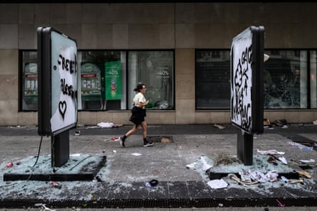 A woman runs past graffiti-covered panels and shattered glass after riots in Lyon