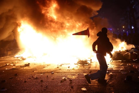 A silhouetted protester throws a traffic cone past a huge burning barricade during Paris demonstrations