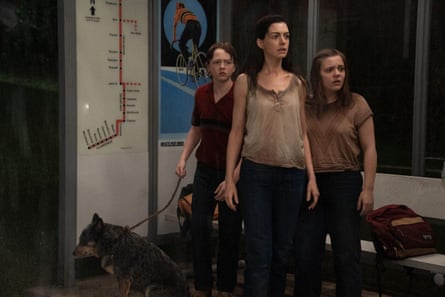Anne Hathaway and two startled girls with a dog stand at a rainy transit stop