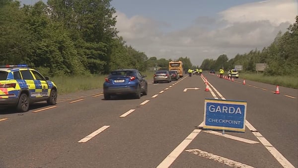 cars are seen driving past a blue sign reading garda checkpoint