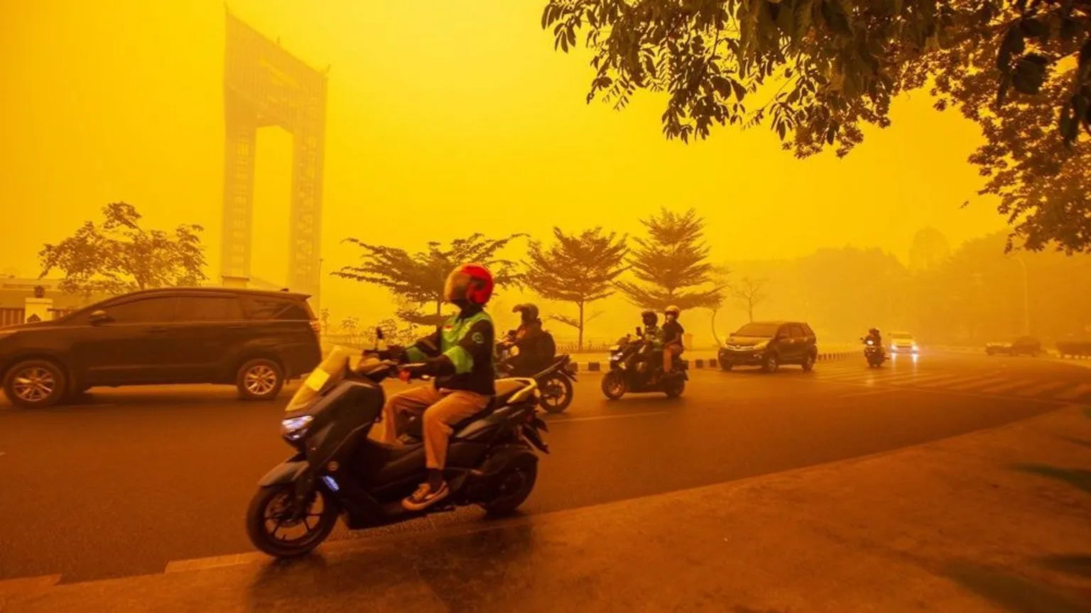 EPA/Shutterstock Motorcyclists and cars travel along a city street shrouded in thick yellow-orange haze