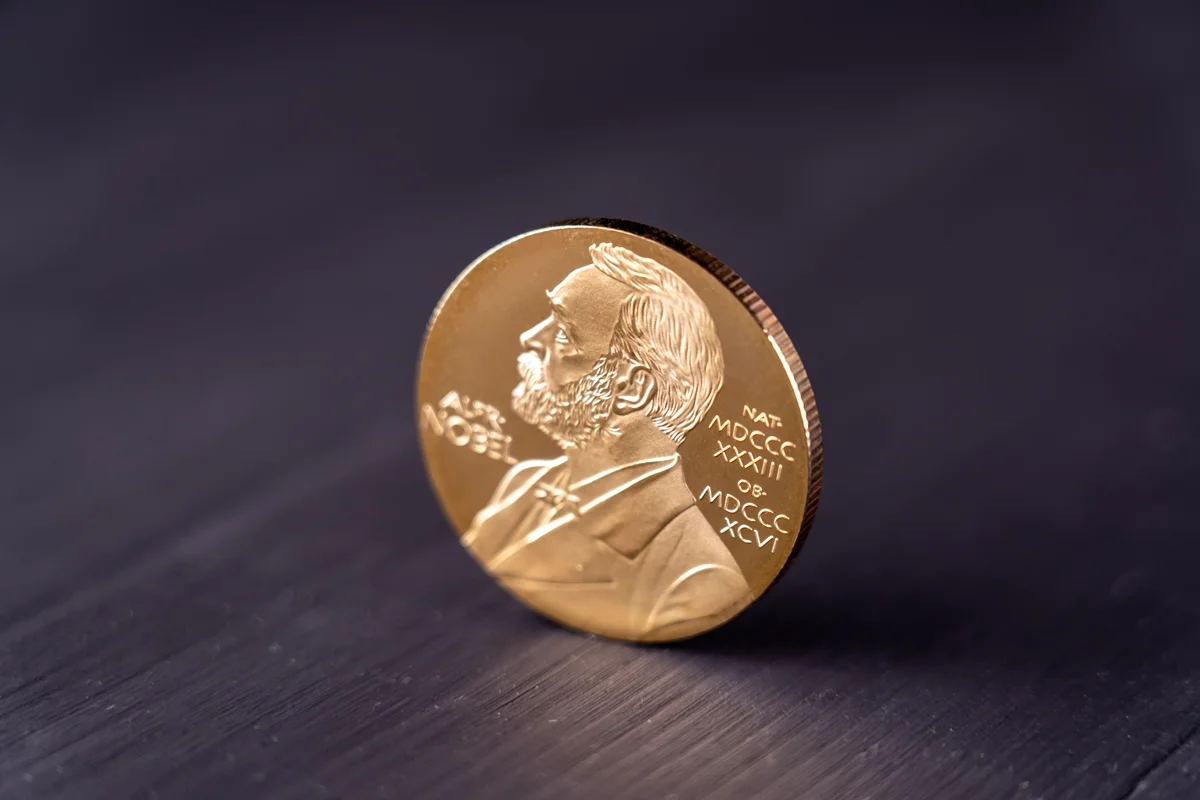Imagem mostra o prêmio Nobel, uma moeda dourada com escritos e a silhueta de um homem - Metrópoles